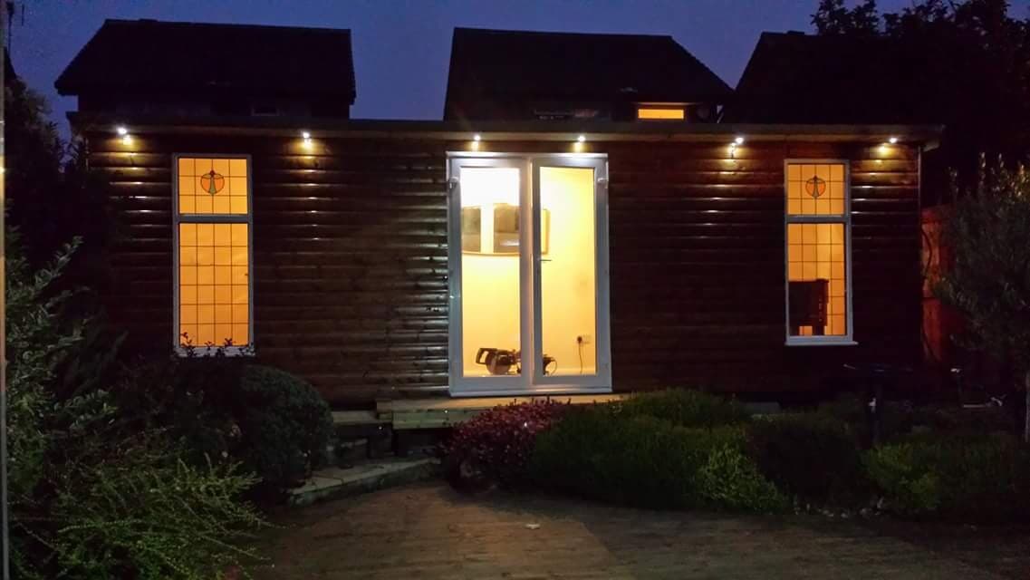 Timber-clad garden room lit at dusk, with lighting set into the soffit and the path and planting lit below
